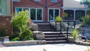Stone steps with glass railing surrounded by landscaping