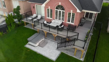 Aerial view of elevated composite deck with frosted glass railings and staircase above a patio and hot tub