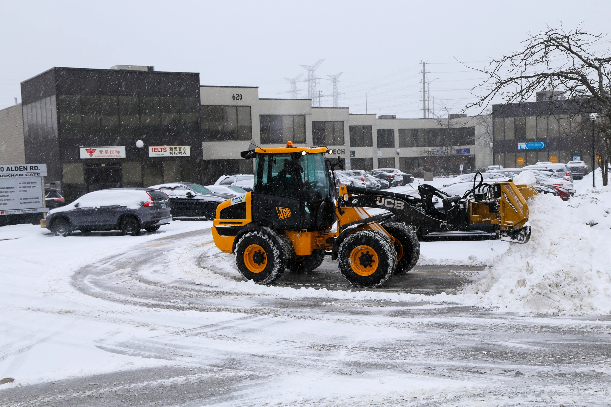 Snow removal tractor plowing a commercial parking lot during snowfall to maintain safety and reduce liability.